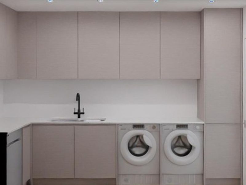 A modern, minimalist laundry room featuring sleek handleless cabinetry, stone countertops, an undermount sink with a black mixer tap, and integrated appliance spaces.