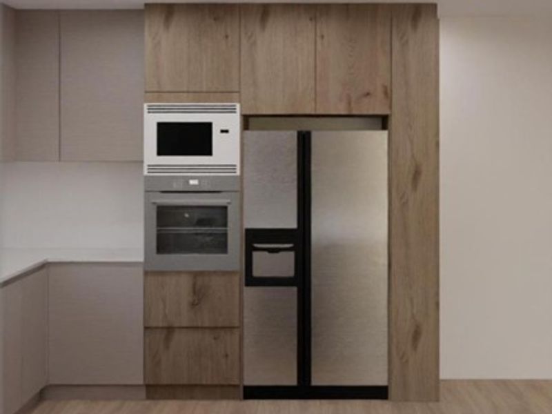 Modern kitchen wall featuring integrated cabinetry, built-in oven, microwave, and space for a large refrigerator with recessed lighting.