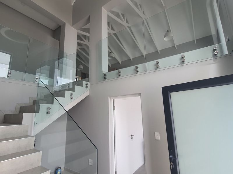 Modern double-volume entrance hall featuring a tiled staircase with glass balustrades, exposed roof trusses, and a contemporary frosted glass front door.