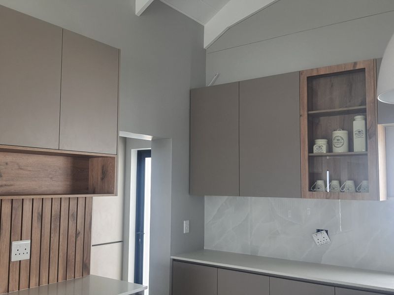 Modern kitchen featuring sleek built-in cabinetry, stone countertops, and decorative slatted wood wall paneling under a high vaulted ceiling.