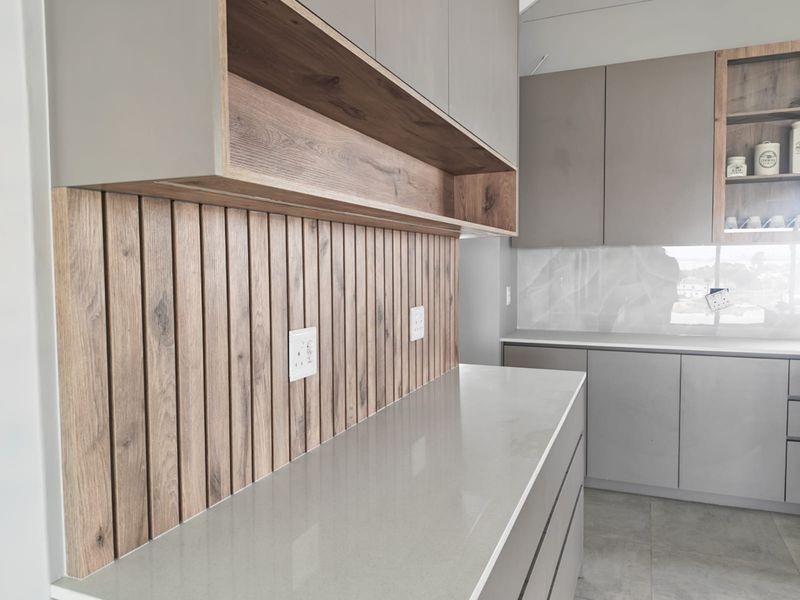 Modern kitchen featuring sleek grey cabinetry, timber slat wall detailing, stone splashback, and high-quality quartz countertops in a clean, contemporary design.