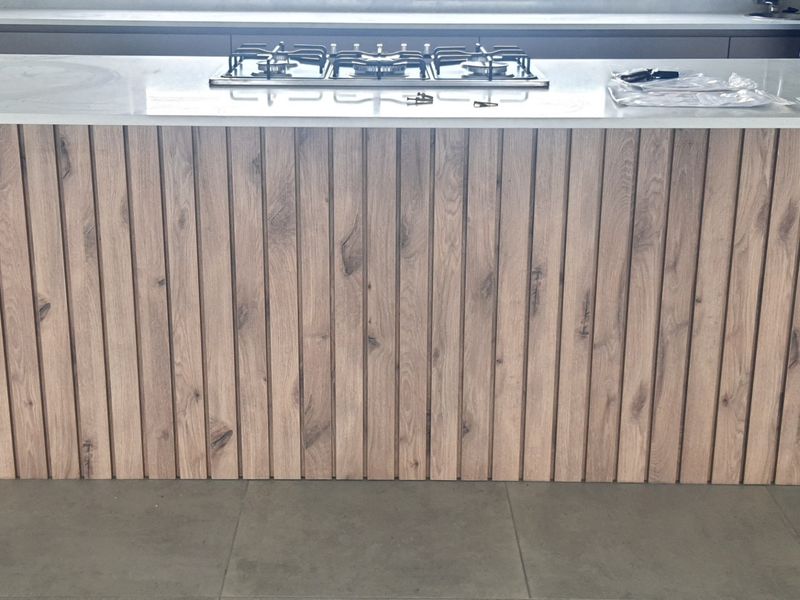Modern kitchen island featuring a stone countertop, integrated gas hob, and stylish timber slat cabinetry finish.