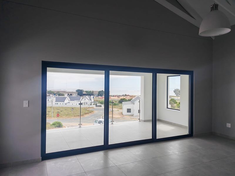 Spacious living area featuring vaulted ceilings, large sliding doors opening to a covered balcony with glass balustrades, and modern tiled flooring.