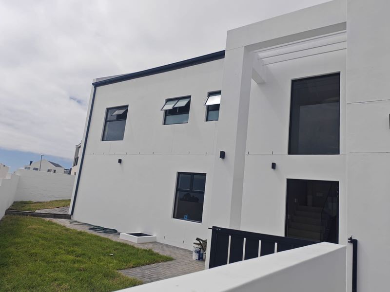 A modern, white-rendered rear exterior elevation featuring clean architectural lines, aluminium-framed windows, and a well-maintained lawn with paved pathways.