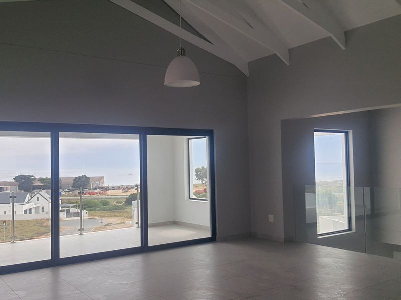 Spacious living area featuring vaulted ceilings with exposed rafters, large sliding doors opening to a balcony, and modern tiled flooring with coastal views.