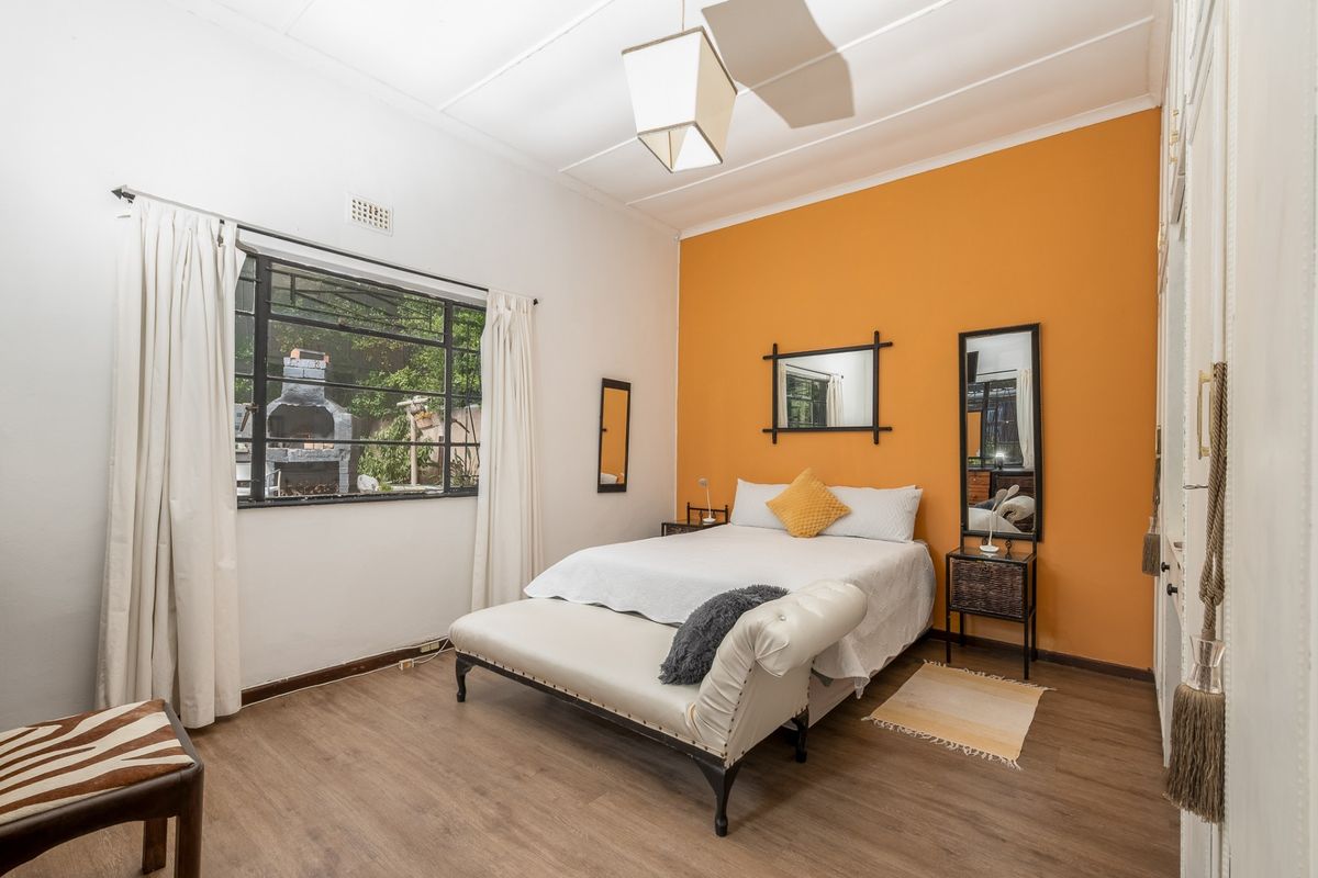 A bedroom featuring laminate flooring, built-in cupboards, and a steel-framed window overlooking the rear garden area.