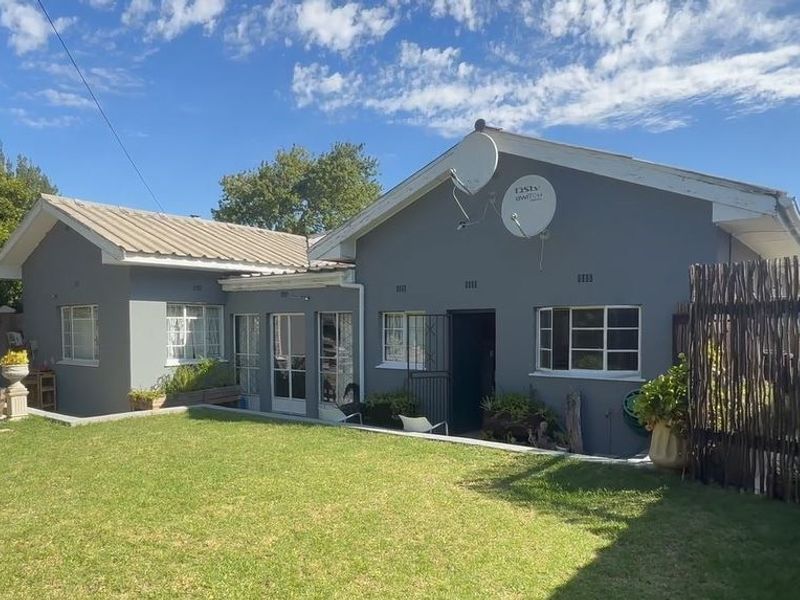 Rear view of the house featuring a metal roof, grey painted exterior walls, and a small lawn area with a retaining wall.