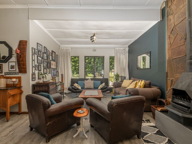 Spacious living room featuring a prominent stone-clad freestanding fireplace, laminate flooring, and large windows providing natural light.