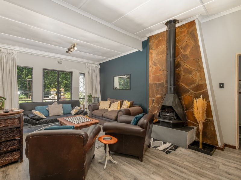 Spacious living room featuring a prominent stone fireplace, laminate flooring, and large windows providing natural light and garden views.