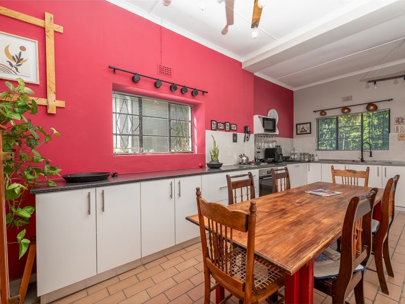 Open-plan kitchen and dining area featuring white cabinetry, dark countertops, built-in appliances, and tiled flooring with a vibrant red feature wall.