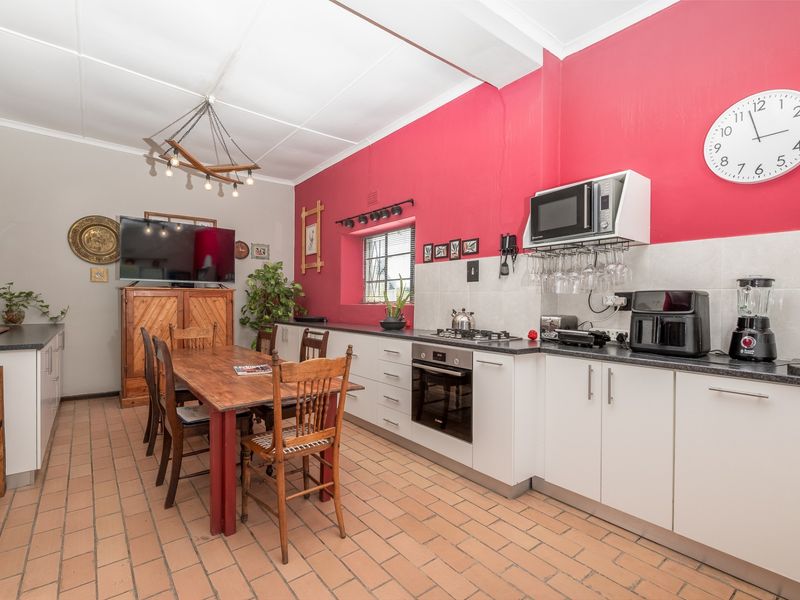 Open-plan kitchen and dining area featuring white cabinetry, built-in oven, gas hob, and tiled flooring with a vibrant accent wall.
