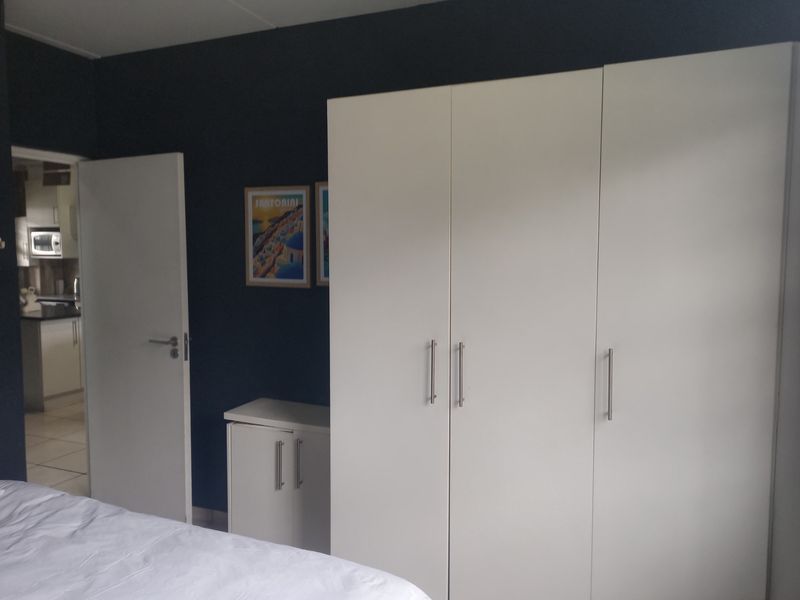 A bedroom featuring a large white built-in wardrobe and dark accent wall, with a view into an adjacent kitchen area.