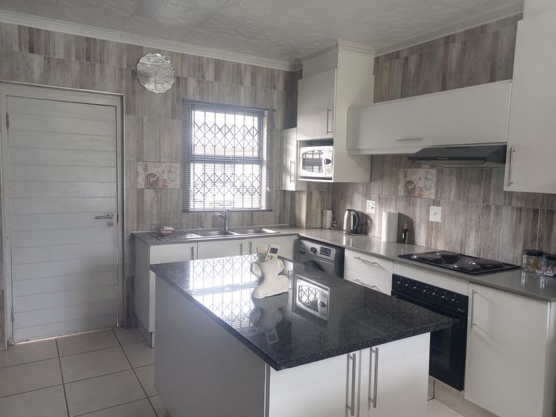 Modern kitchen featuring a central island with granite countertops, built-in oven, hob, extractor fan, and ample cabinetry, complemented by tiled flooring and a security gate.