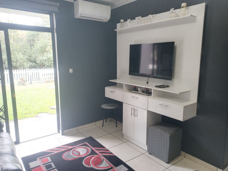 A living room featuring tiled flooring, a built-in media console, a wall-mounted air conditioner, and direct access to an outdoor garden area via sliding doors.