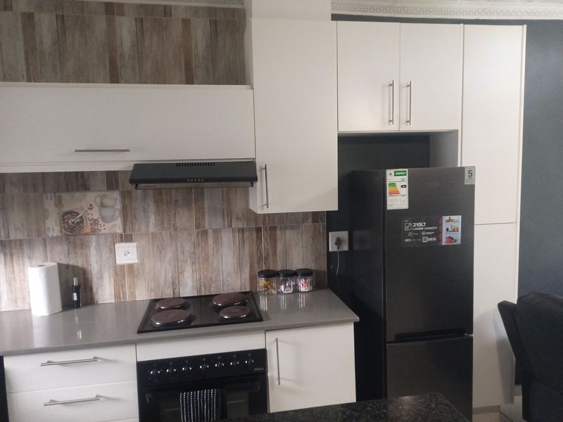 Modern kitchen featuring white cabinetry, stone countertops, tiled backsplash, and integrated appliances including an electric hob and oven.