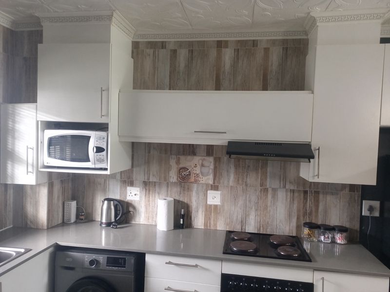 A functional kitchen featuring modern white cabinetry, wood-look tiled backsplash, stone countertops, and integrated appliances including a hob, oven, and microwave.