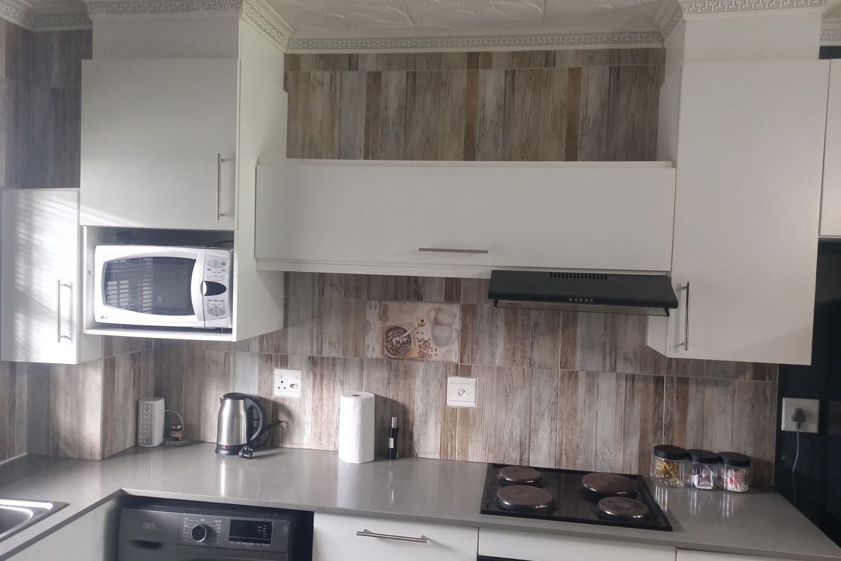 A functional kitchen featuring modern white cabinetry, wood-look tiled backsplash, stone countertops, and integrated appliances including a hob, oven, and microwave.