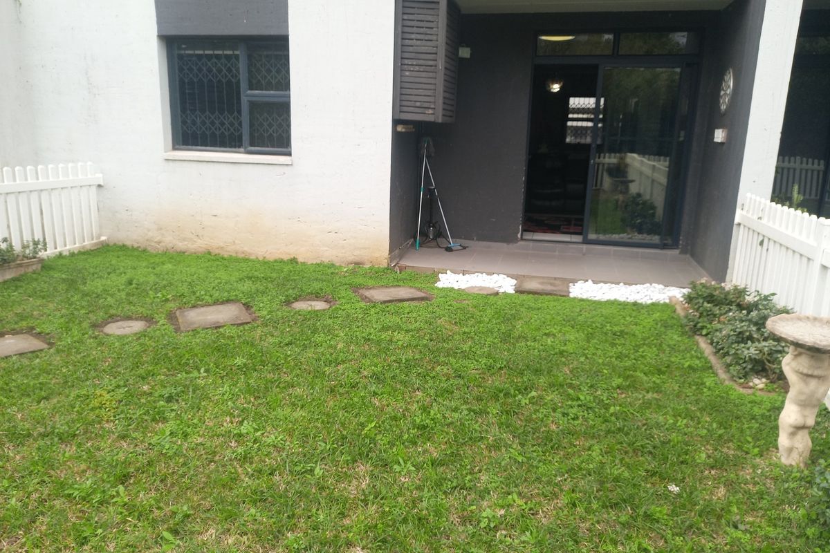 Rear exterior view of the apartment featuring a small private garden, white picket fencing, and a tiled patio area with sliding door access.