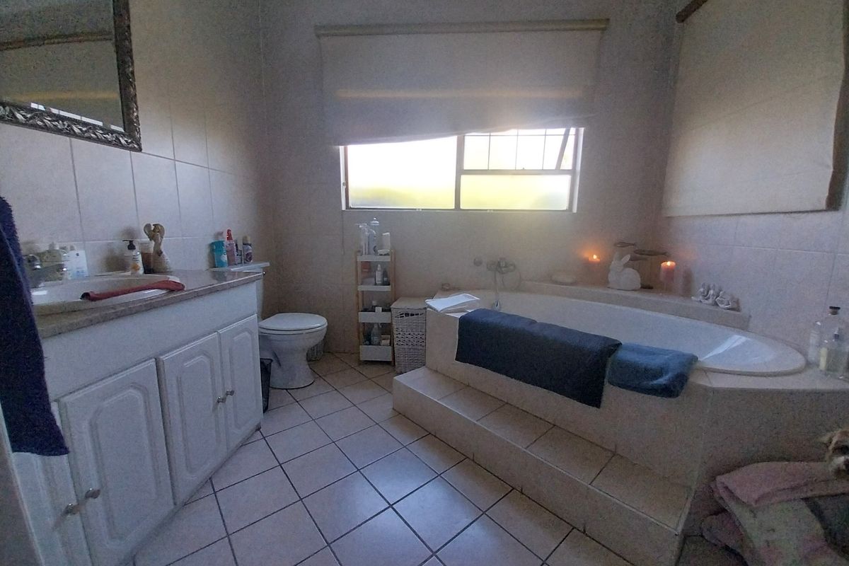A functional bathroom featuring a built-in vanity with basin, a tiled drop-in bathtub, and neutral wall and floor tiling.