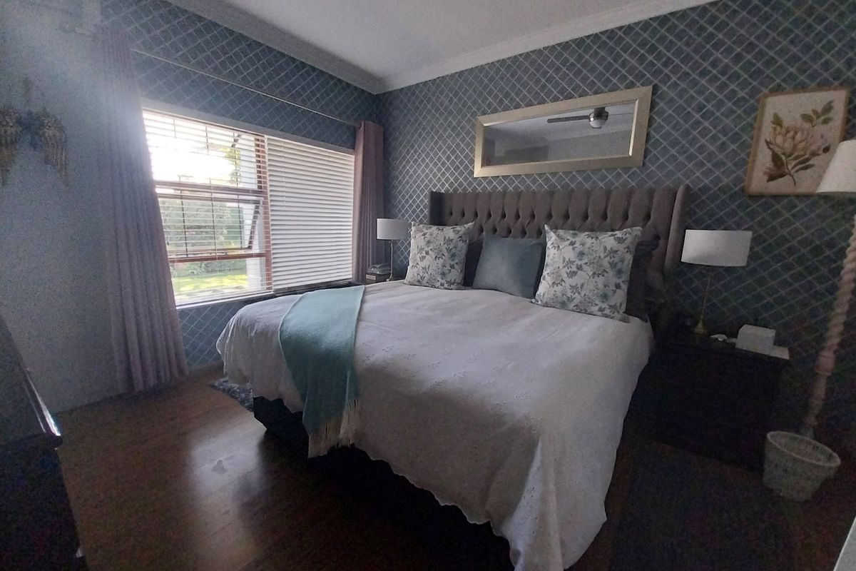 A well-maintained bedroom featuring laminate flooring, crown molding, and a ceiling fan, with large windows fitted with venetian blinds for natural light.