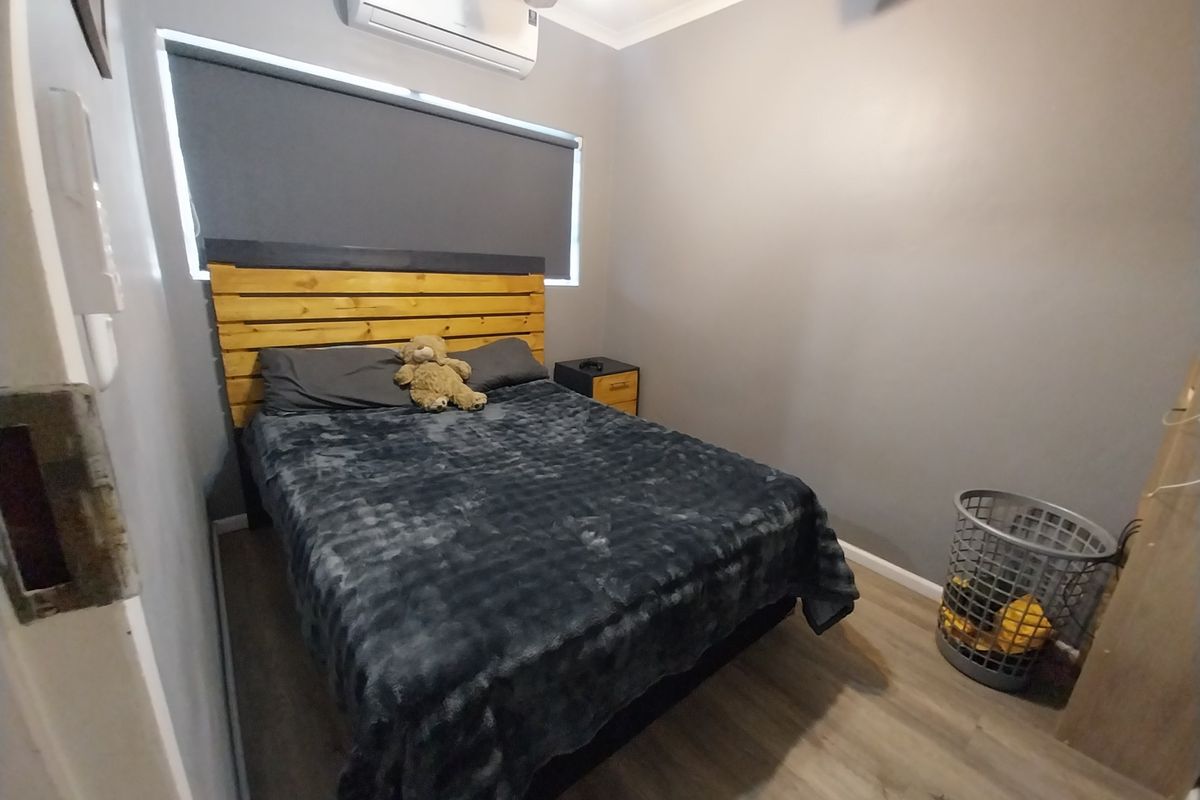 A compact bedroom featuring laminate flooring, a ceiling fan, and a wall-mounted split-system air conditioner.