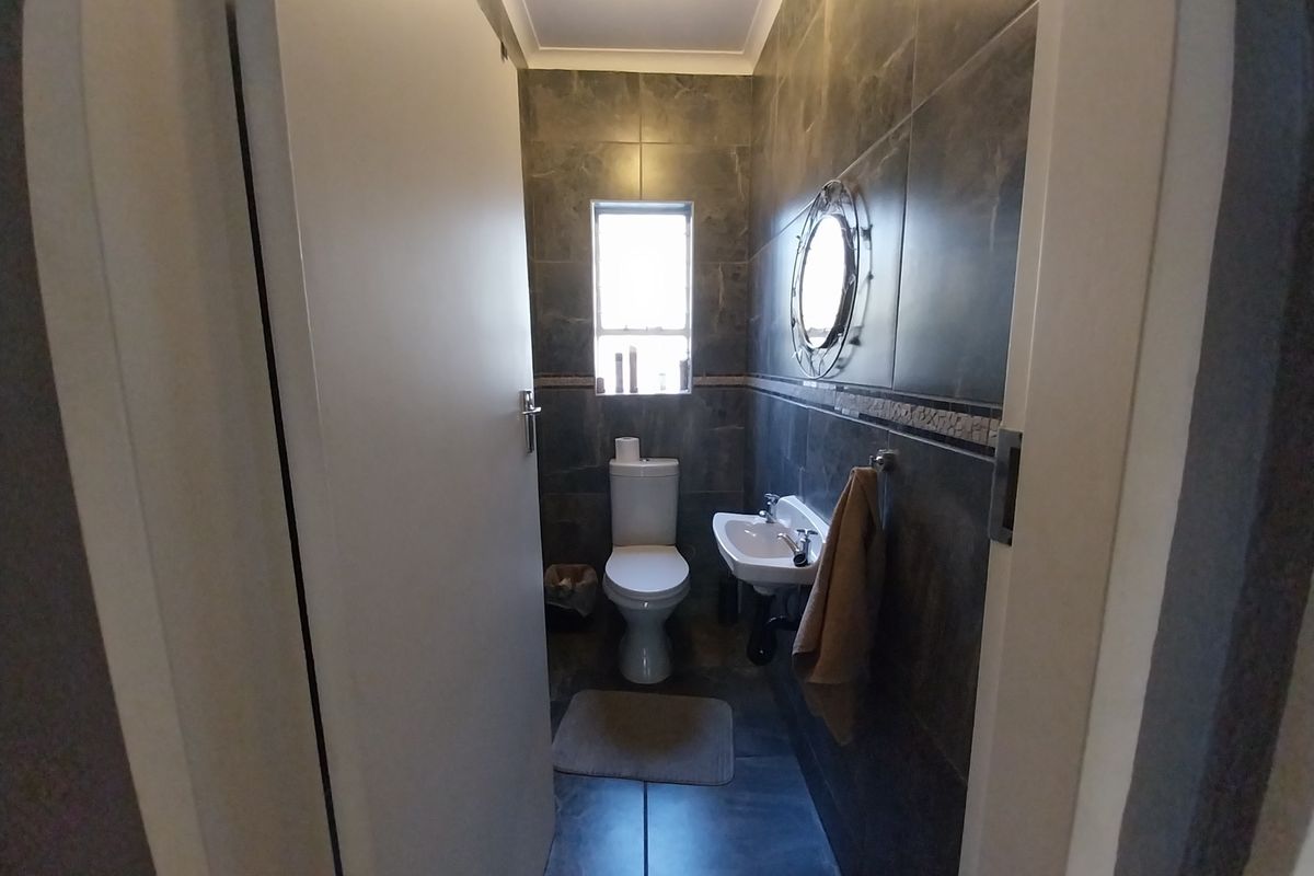 A compact bathroom featuring dark tiled walls, a wall-mounted basin, and a standard toilet.