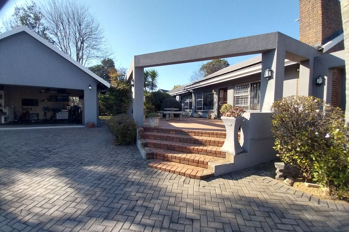 Rear exterior view featuring a brick paved patio with steps, a detached garage, and a brick chimney structure.