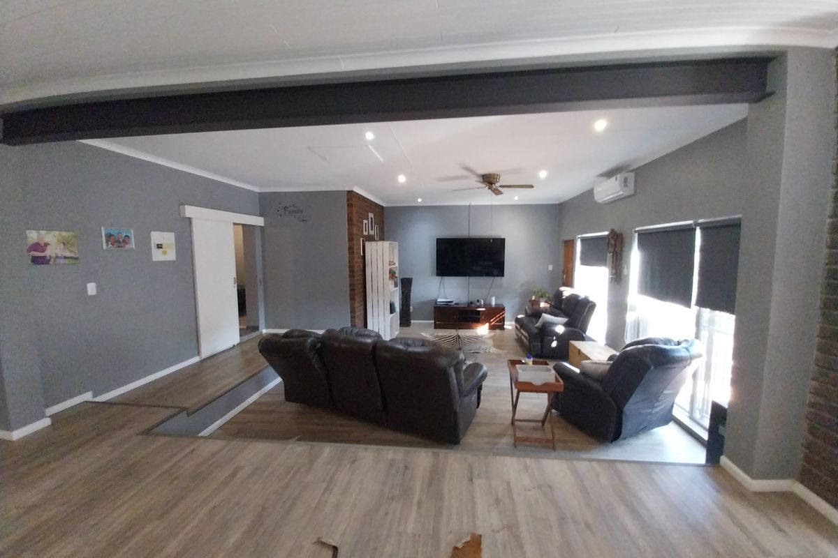 Spacious open-plan living area featuring a modern exposed steel beam, laminate flooring, recessed lighting, and a brick feature wall.
