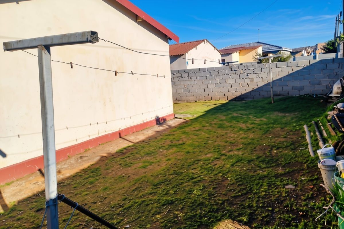 Rear garden area featuring a concrete block boundary wall and a metal washing line pole, with patchy lawn and exposed soil.