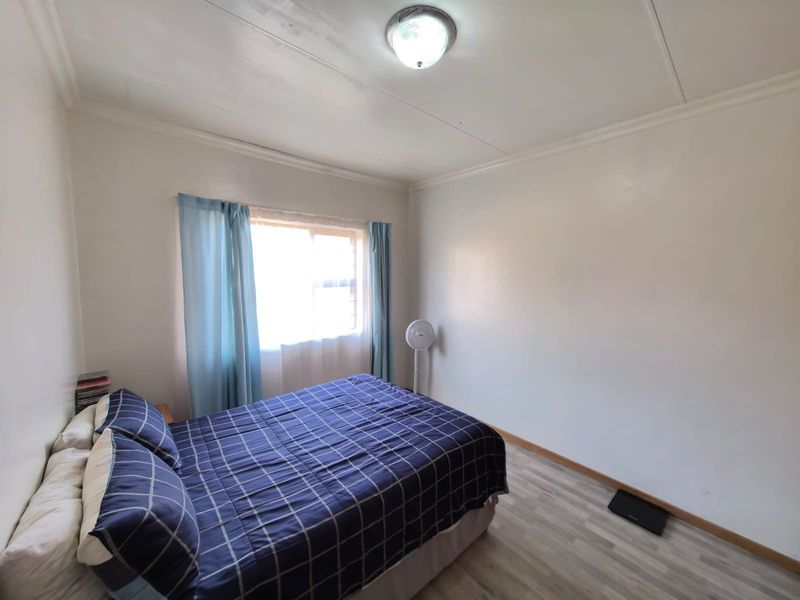 A simple bedroom featuring laminate flooring and a window, showing signs of ceiling water damage that may require maintenance.