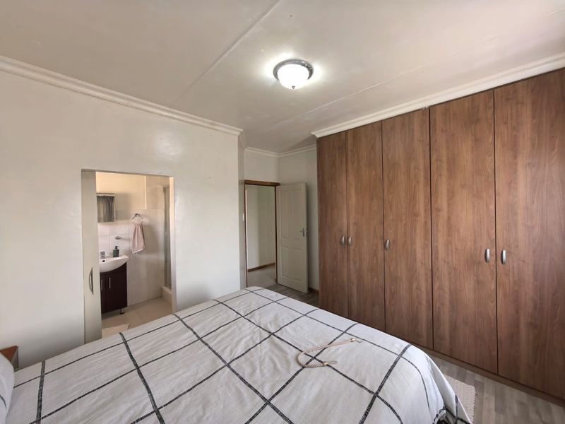 A well-maintained bedroom featuring extensive built-in wooden cupboards and direct access to an en-suite bathroom.
