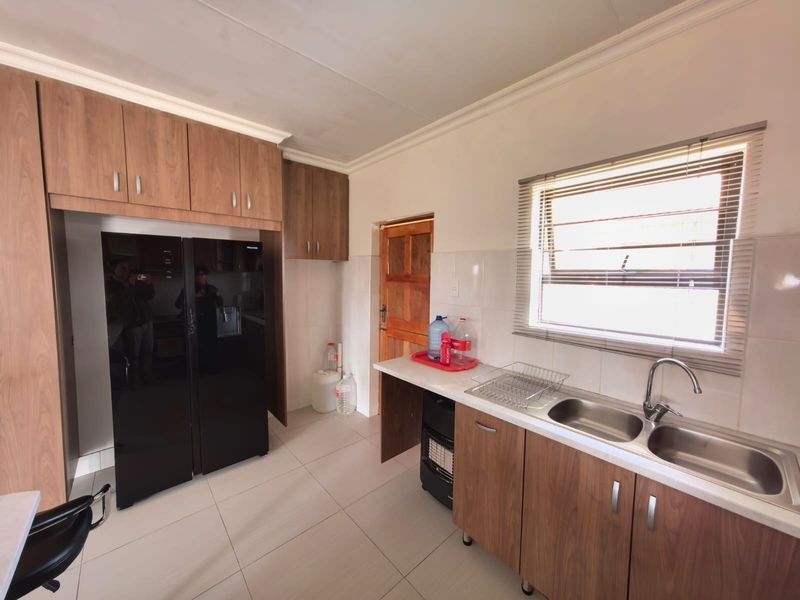A functional kitchen featuring wood-finish cabinetry, a double stainless steel sink, tiled splashbacks, and neutral floor tiles.