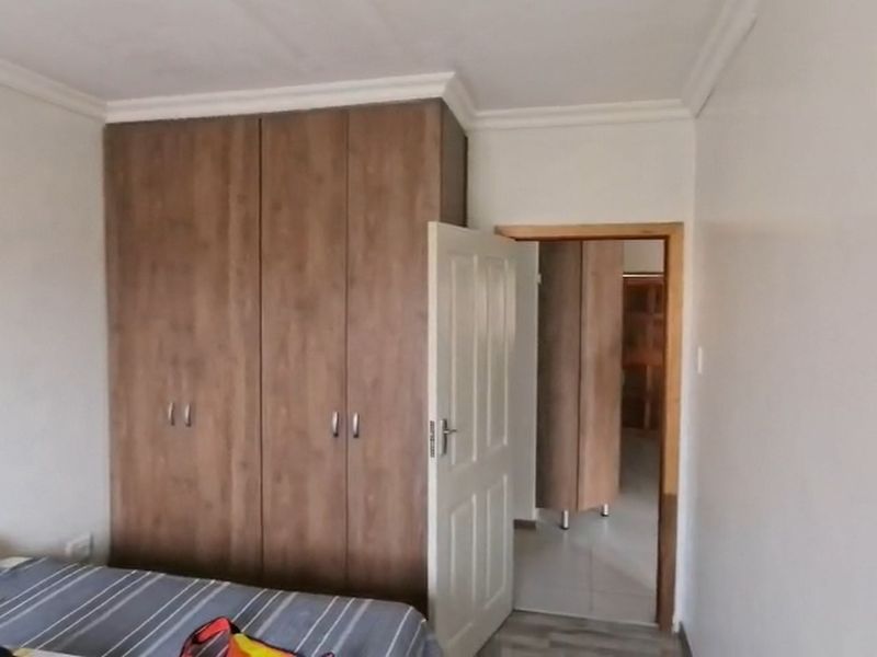 A bedroom featuring built-in wooden cupboards and decorative ceiling cornicing, with an open doorway leading to an adjacent room.