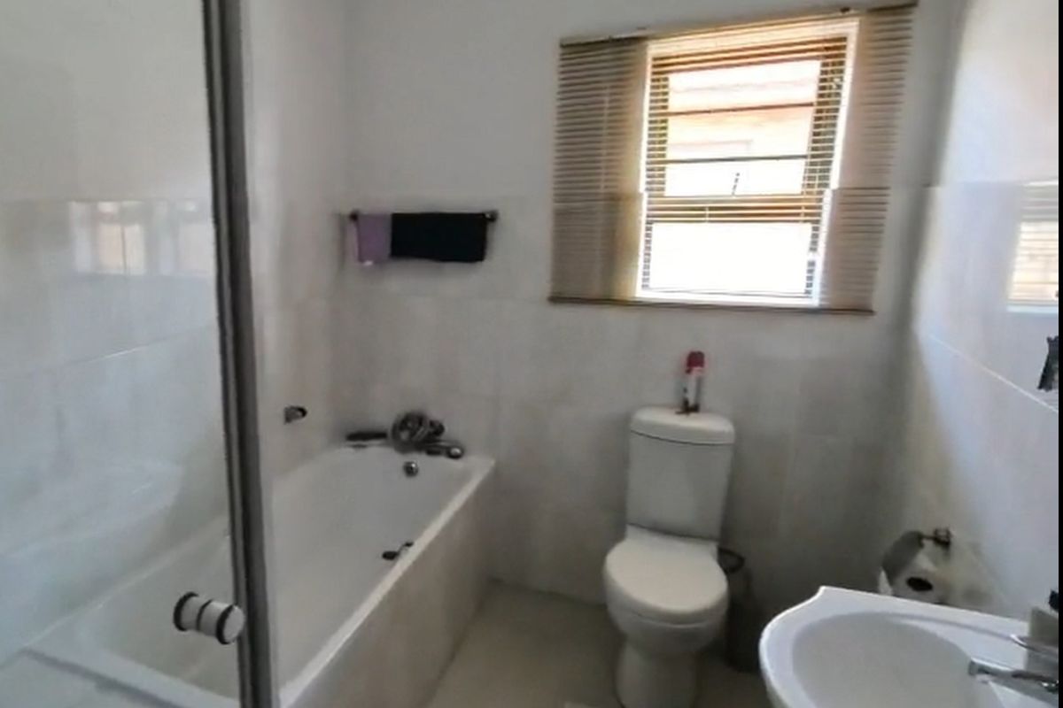 A functional bathroom featuring a bathtub, glass shower screen, pedestal basin, and toilet with neutral wall and floor tiling.
