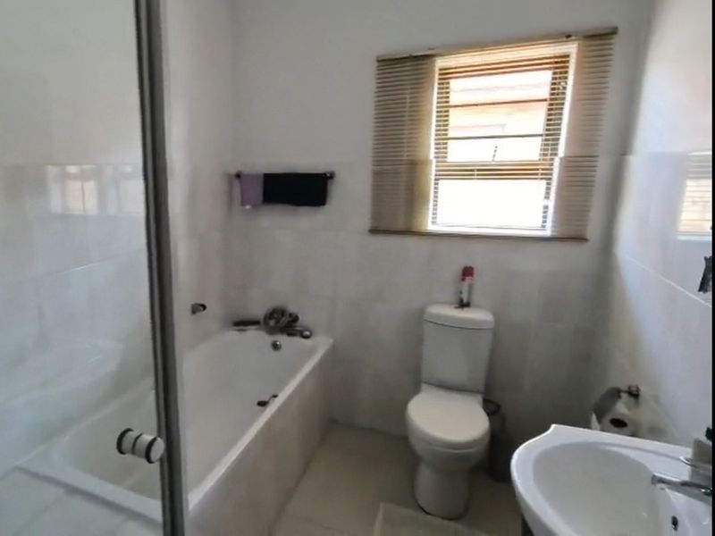 A functional bathroom featuring a bathtub, glass shower screen, pedestal basin, and toilet with neutral wall and floor tiling.