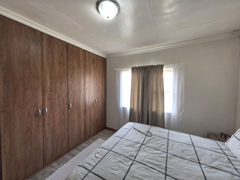A bedroom featuring extensive built-in wooden cupboards, laminate flooring, and a central ceiling light fixture.