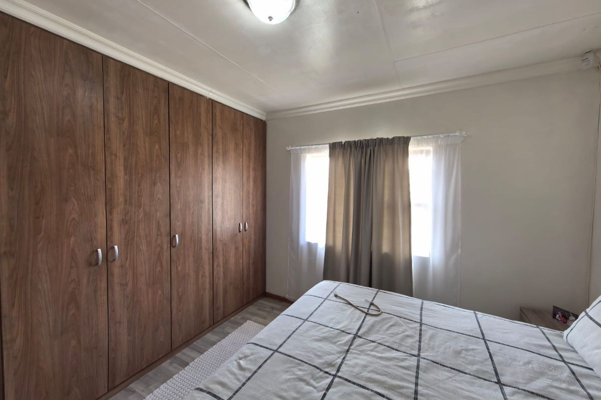 A bedroom featuring extensive built-in wooden cupboards, laminate flooring, and a central ceiling light fixture.