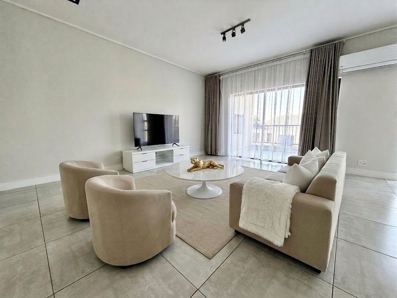 A bright and modern living room featuring large format floor tiles, a wall-mounted air conditioning unit, and direct access to a balcony through sliding doors.