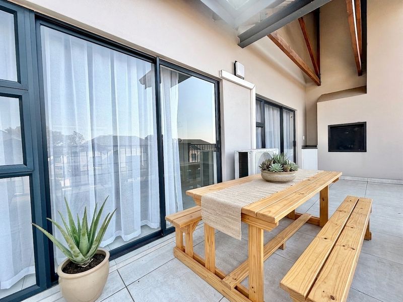 Spacious covered balcony featuring tiled flooring, exposed timber rafters, a built-in fireplace, and large sliding glass doors providing seamless indoor-outdoor flow.