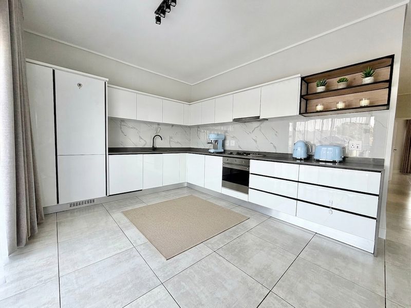 Modern kitchen featuring sleek white cabinetry, marble-look splashback, integrated oven, hob, and extractor fan with contemporary black fixtures and tiled flooring.