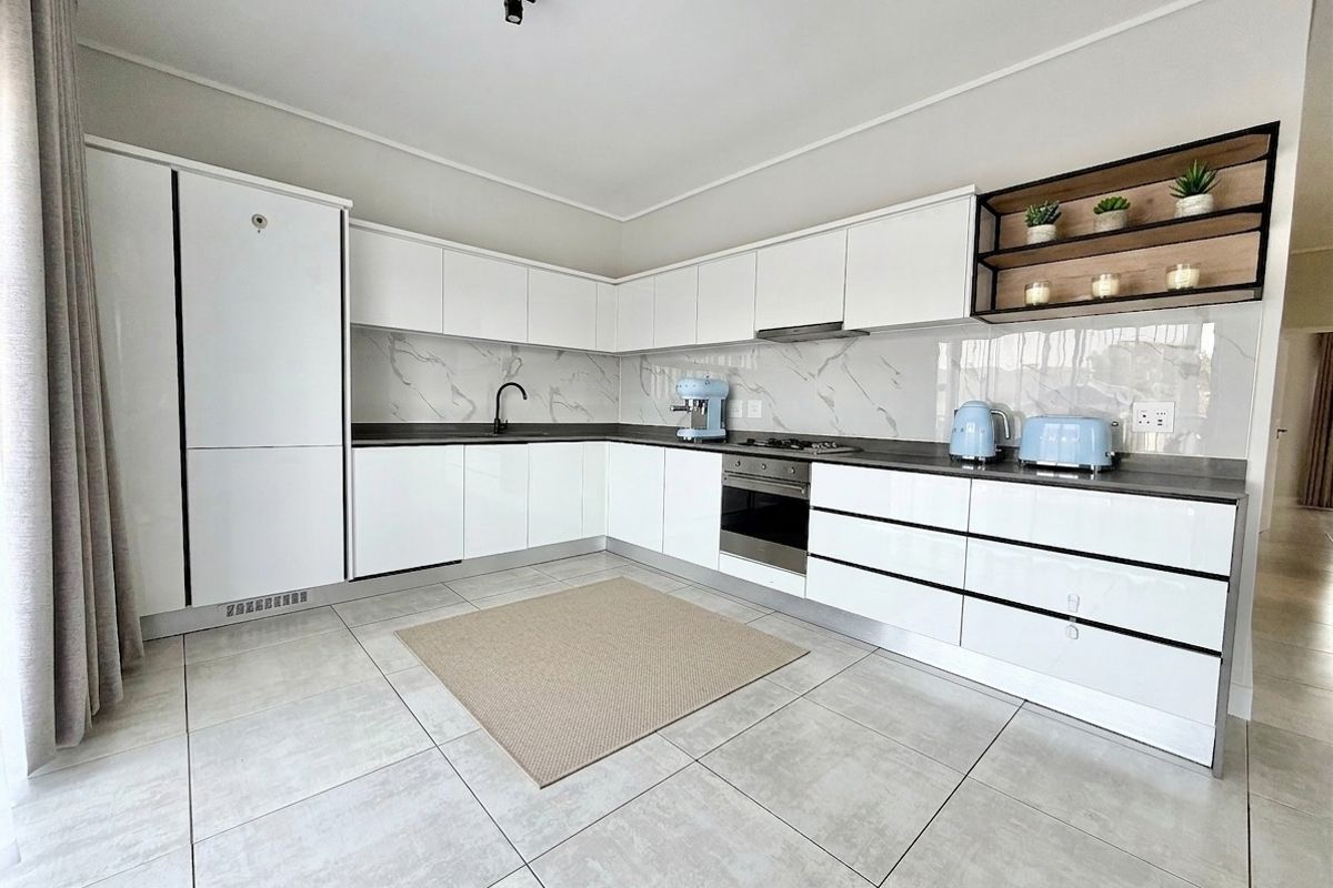 Modern kitchen featuring sleek white cabinetry, marble-look splashback, integrated oven, hob, and extractor fan with contemporary black fixtures and tiled flooring.