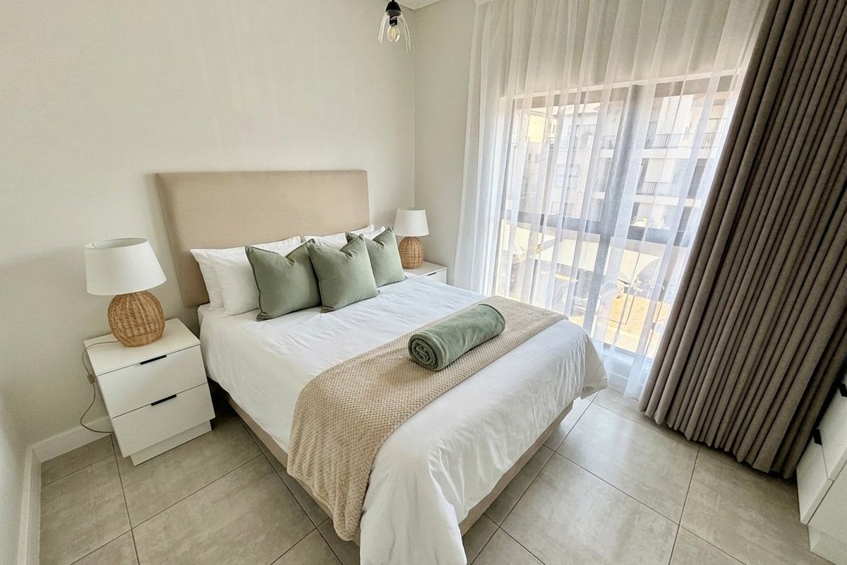 A well-maintained bedroom featuring neutral tiled flooring, a large window with floor-to-ceiling curtains, and modern pendant lighting.