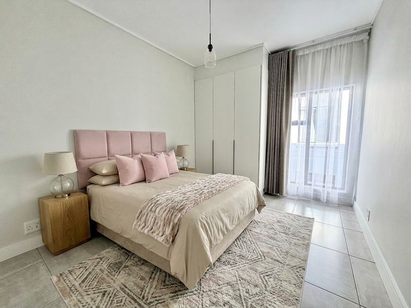 Modern bedroom featuring built-in cupboards, neutral tiled flooring, and a sliding glass door providing natural light.