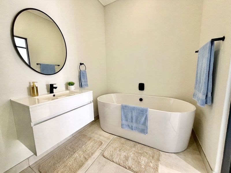 Modern bathroom featuring a sleek freestanding bathtub, wall-mounted vanity with integrated basin, and contemporary black fixtures.