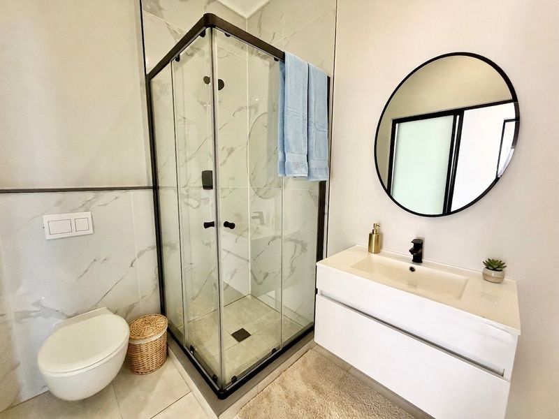 Modern bathroom featuring a glass shower enclosure, wall-mounted toilet, and a sleek vanity with black matte fixtures and marble-look wall tiling.