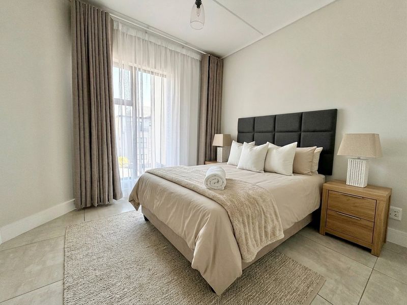 A well-maintained bedroom featuring neutral tiled flooring, a large sliding glass door with floor-to-ceiling curtains, and a modern pendant light fixture.