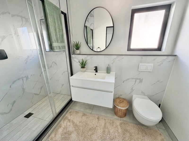Modern bathroom featuring a walk-in shower with black frame, wall-mounted vanity, wall-hung toilet with concealed cistern, and elegant marble-look wall tiling.