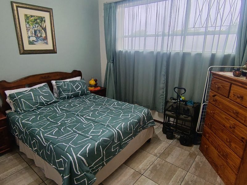 A functional bedroom featuring tiled flooring and a large window with security bars, providing natural light.