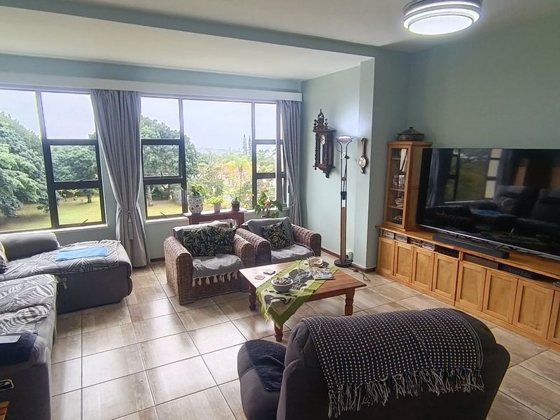 A spacious living room featuring large aluminium-framed windows that provide natural light and views, complemented by tiled flooring throughout.