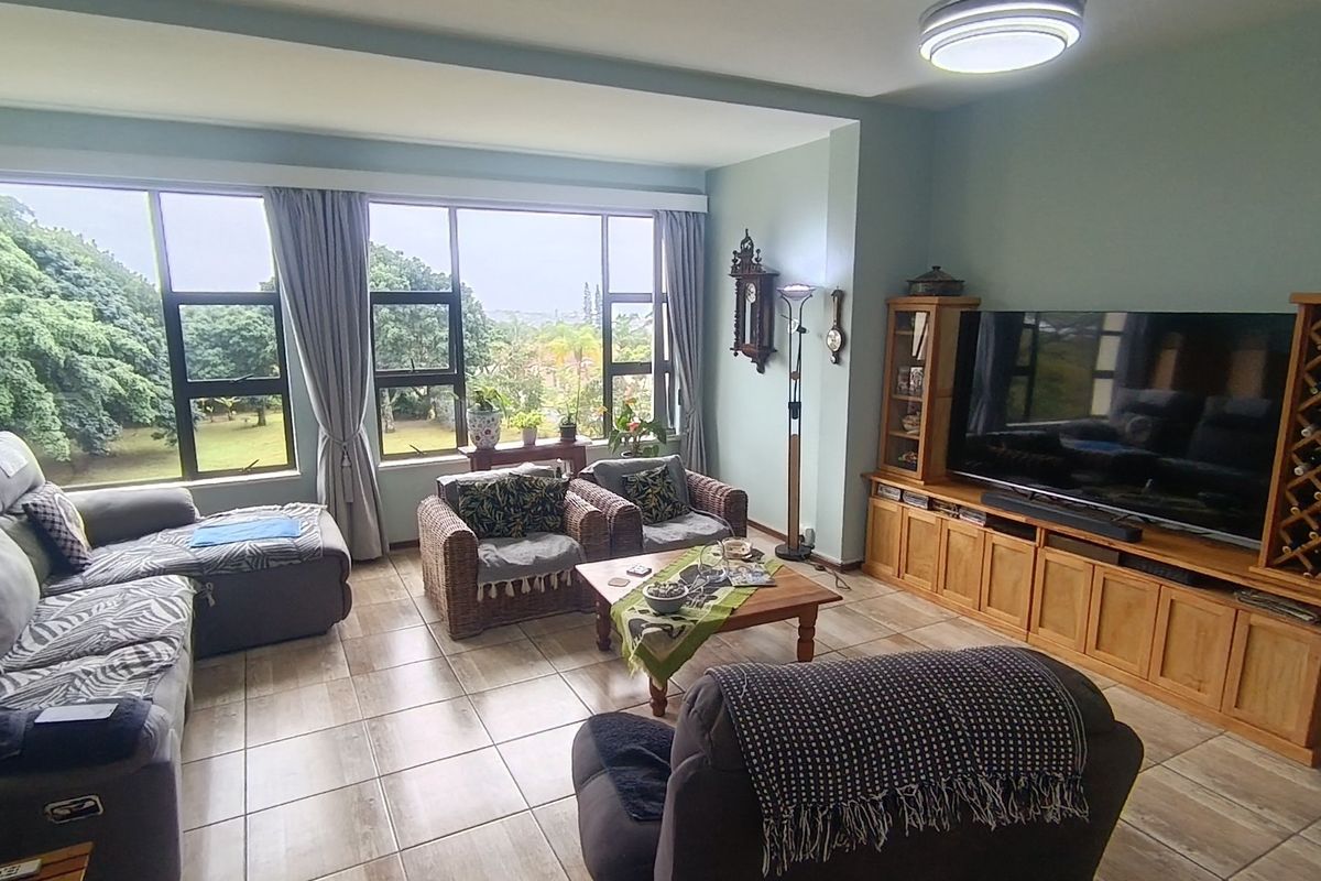 A spacious living room featuring large aluminium-framed windows that provide natural light and views, complemented by tiled flooring throughout.